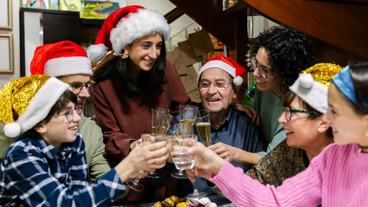 Group of friends and family wearing Santa hats, toasting with champagne glasses at a festive Christmas gathering.